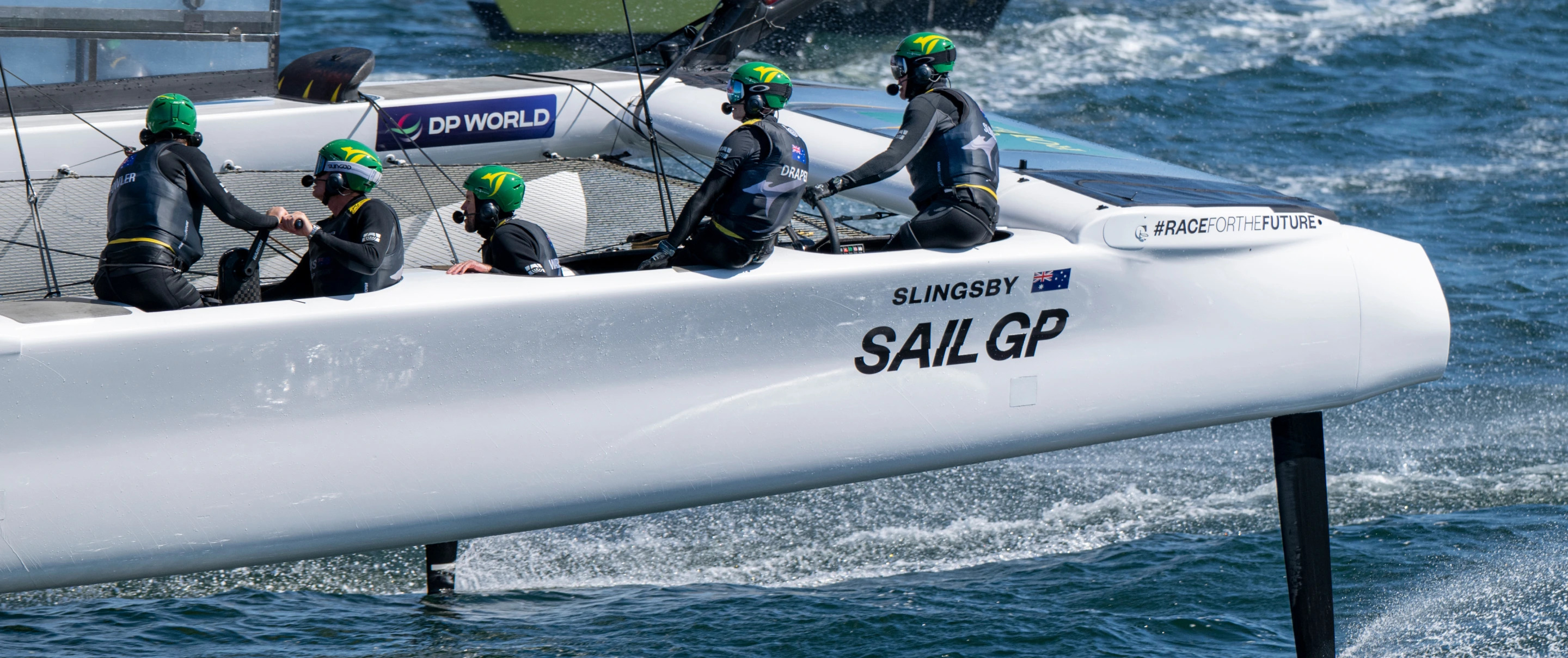 crew members in sleek black wetsuits and green helmets maneuver the Slingsby SailGP sailboat during a race.